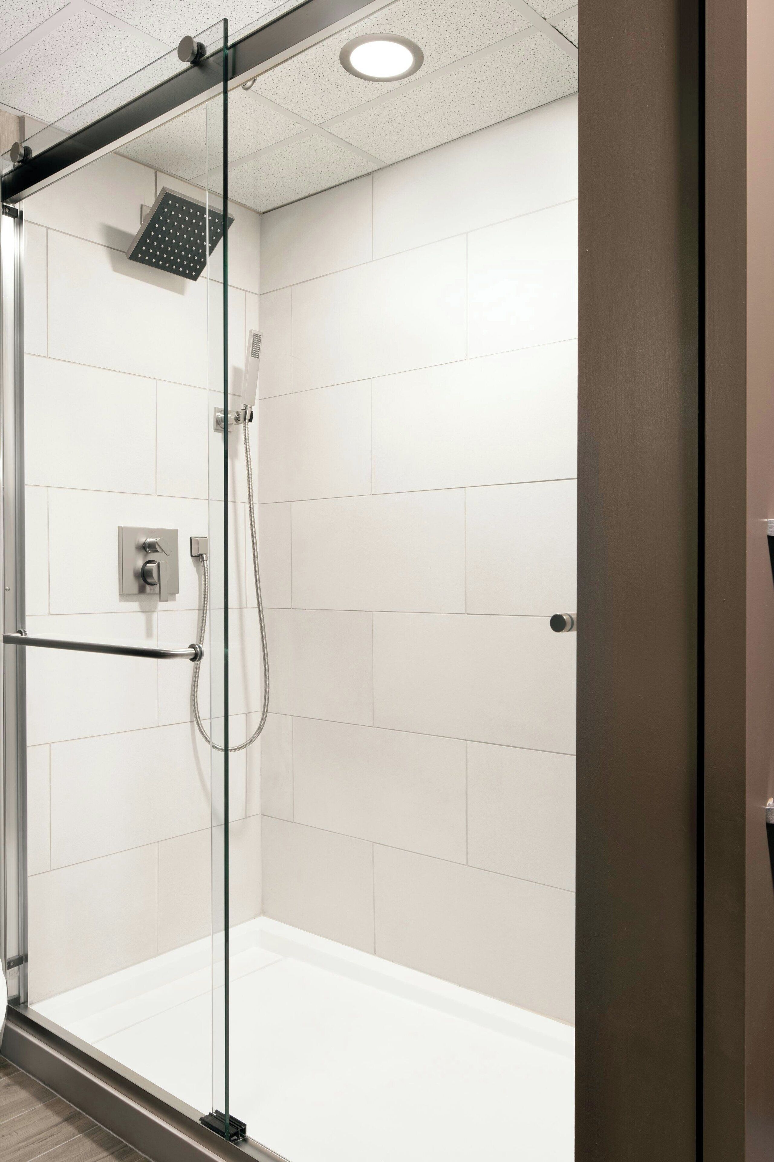 Ducha moderna con mampara de vidrio, paredes de azulejos blancos y panel de control.