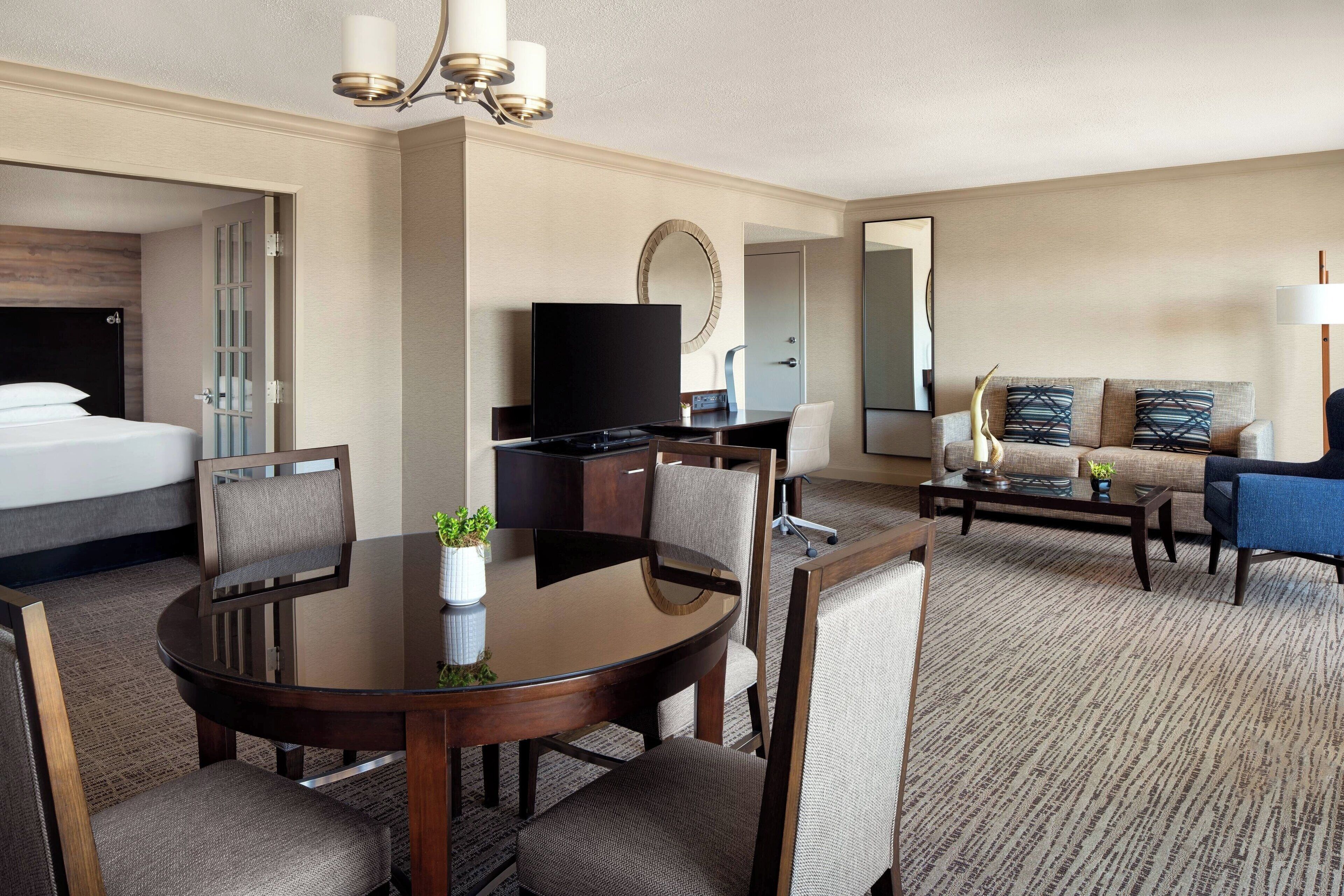 Una habitación de hotel con una cama, televisión, mesa de comedor con sillas, sofá y una mesa de centro.