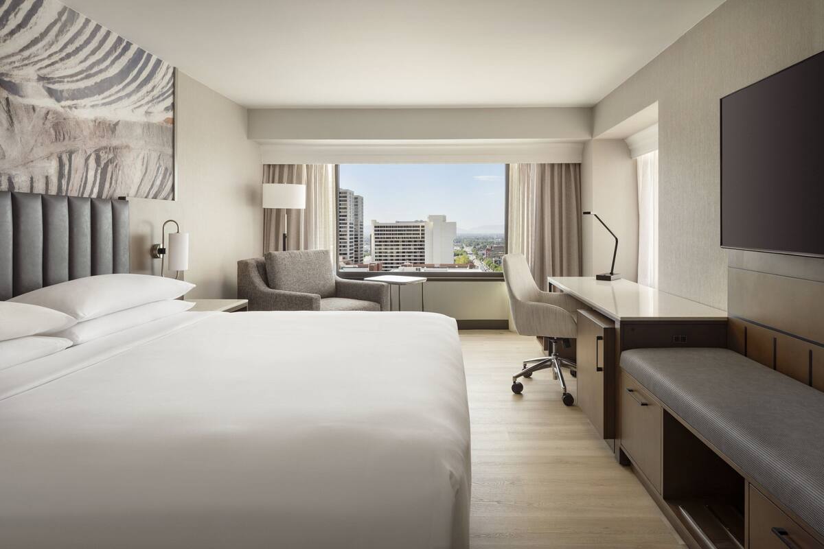 Quarto de hotel moderno com uma cama grande, uma escrivaninha, uma cadeira e uma televisão.