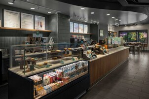 L'intérieur d'un café présente un comptoir où sont exposées des pâtisseries et des boissons, un panneau affichant le menu au-dessus du comptoir, et un espace salon avec des tables et des chaises.