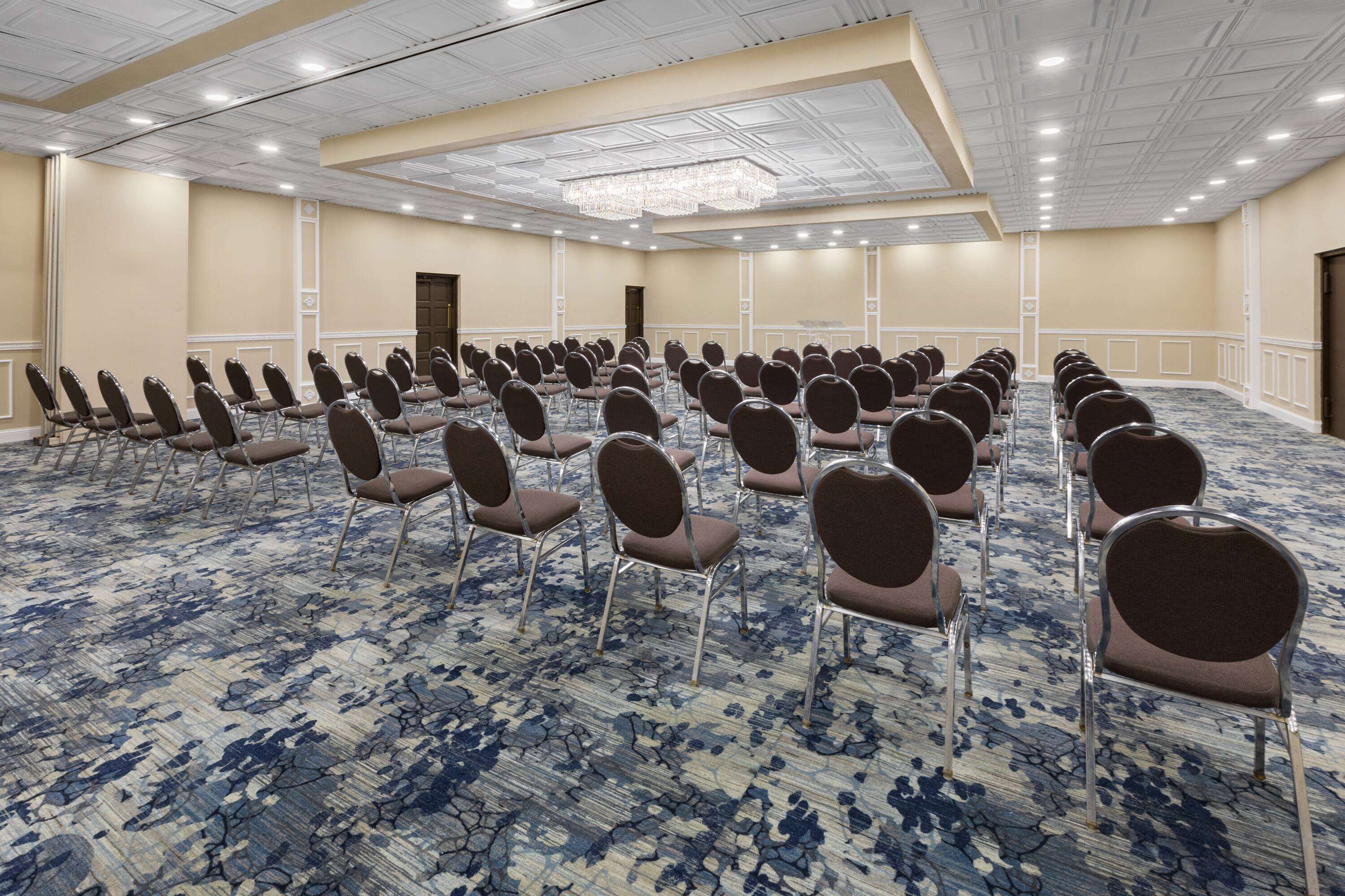 Une grande salle de conférence avec des rangées de chaises, une moquette à motifs et un lustre.