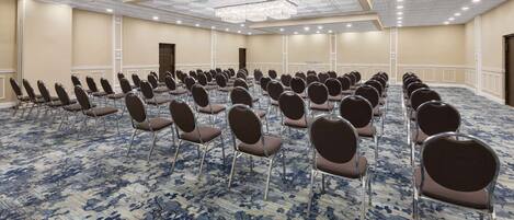 Une grande salle de conférence avec des rangées de chaises, une moquette à motifs et un lustre.