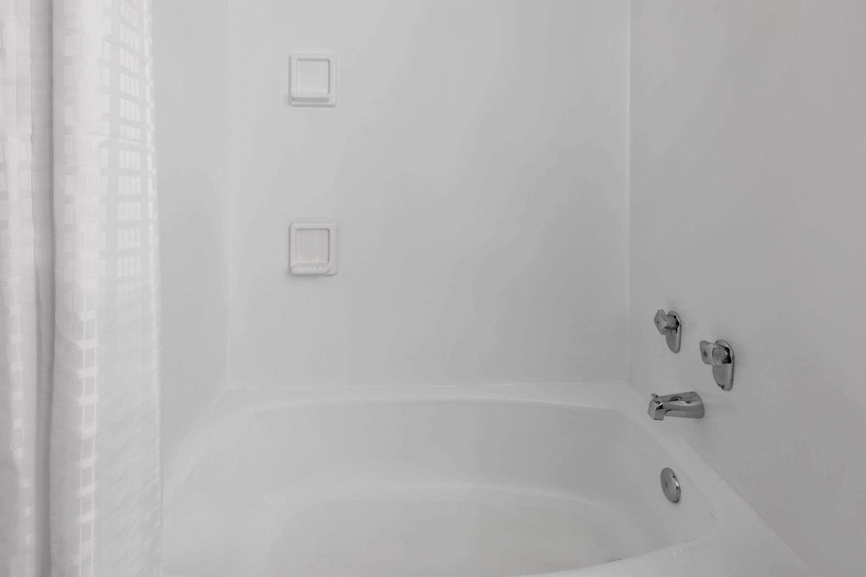 A white bathtub with a shower curtain, a wall-mounted faucet, and a handheld showerhead.