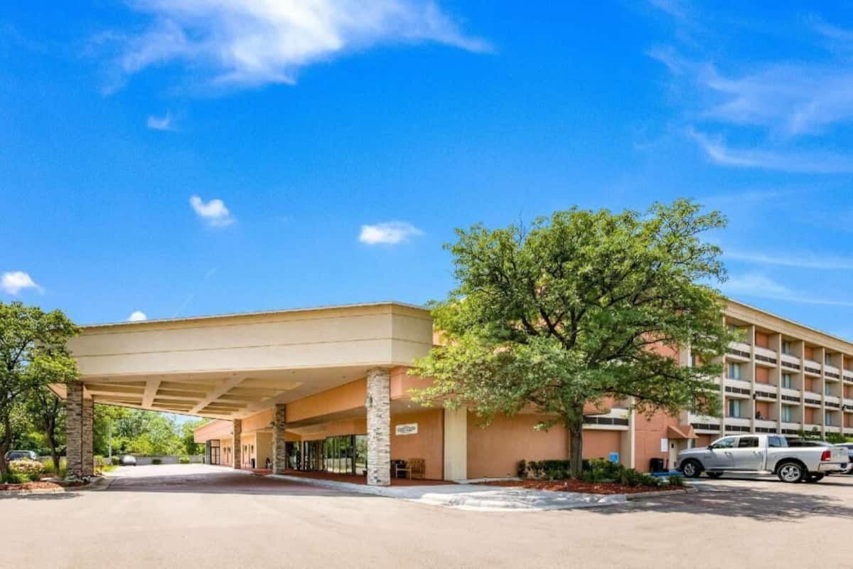 Un hotel con entrada cubierta, aparcamiento y un árbol en la parte delantera.