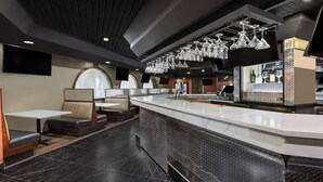 Ein modernes Restaurant-Interieur mit einer langen Theke, Sitzgelegenheiten und dekorativem Glas, das von der Decke hängt.