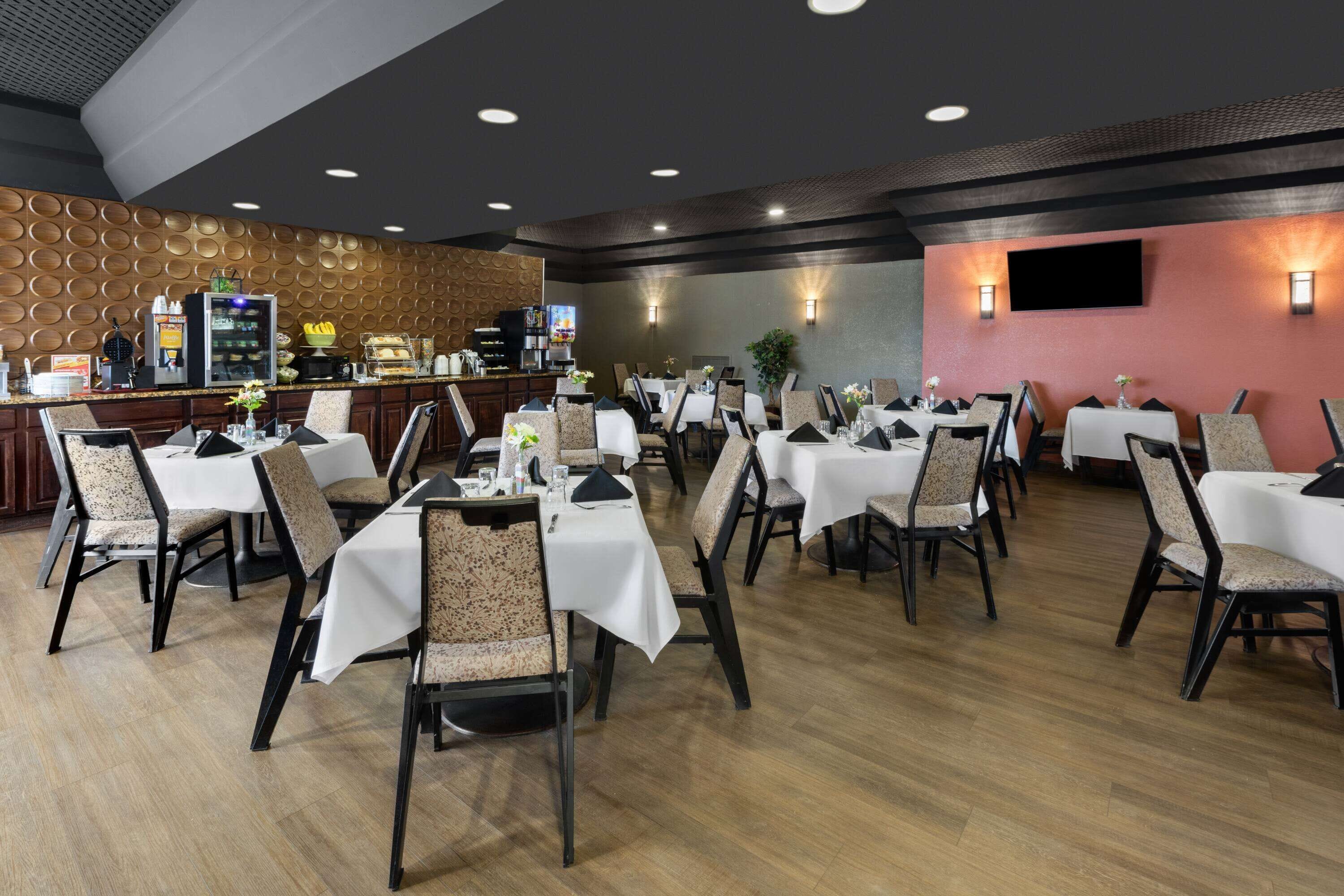 En restaurant med flere borde og stole, en disk med menu og et fjernsyn ophængt på væggen.