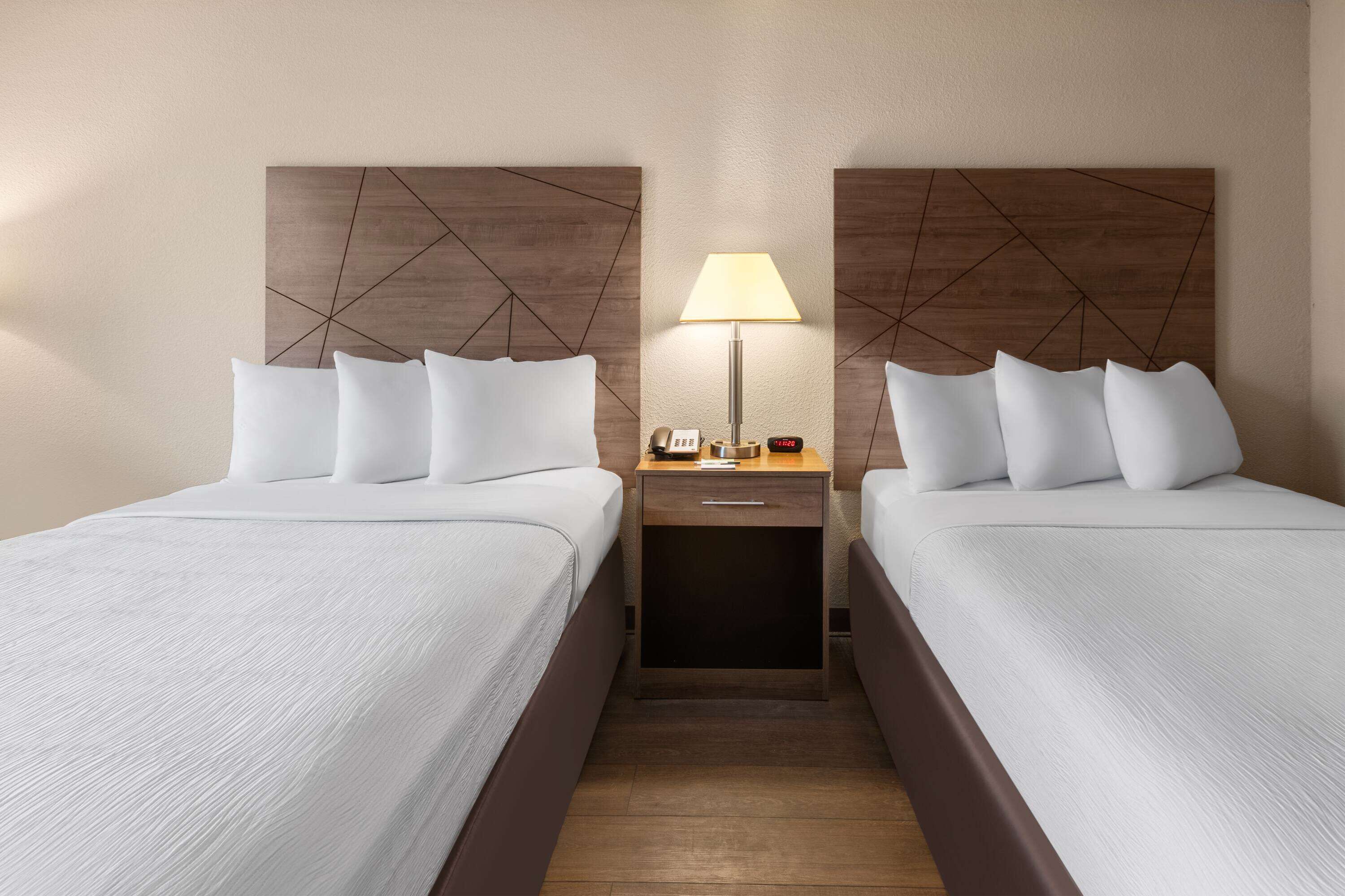 A hotel room with two beds, a nightstand with a lamp, and a clock.