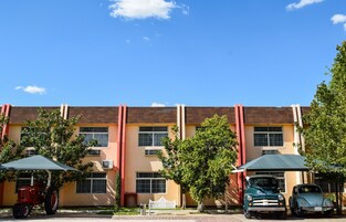 Un edificio con techo plano, varias ventanas y un estacionamiento con dos autos antiguos y un tractor.