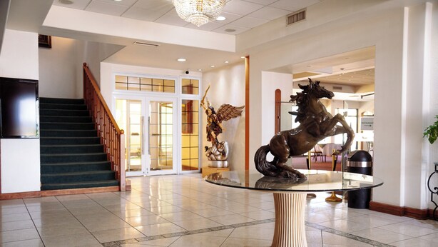 A lobby with a staircase, a glass table with a bronze horse sculpture, and a reception area in the background.