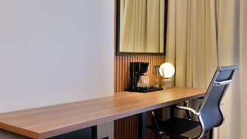 Una habitación de hotel moderna con un escritorio de madera, una silla de oficina negra, una cafetera y una lámpara.