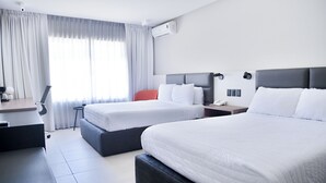 A hotel room with two beds, a desk, a chair, and an air conditioning unit.