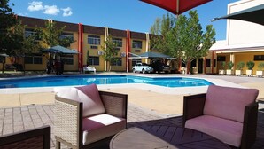 A swimming pool with lounge chairs and umbrellas, surrounded by buildings with yellow and red facades.