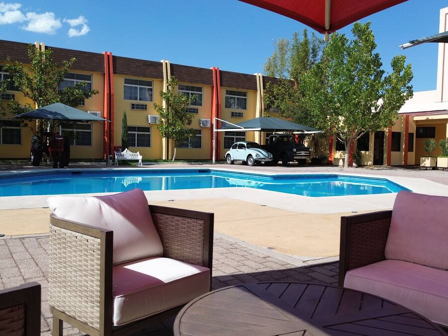 Una piscina con sillones de playa y sombrillas, rodeada de edificios con fachadas amarillas y rojas.