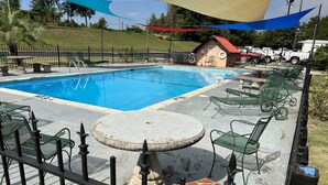 Piscina com espreguiçadeiras e um pequeno edifício ao fundo.