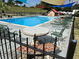 Una piscina con sillones de descanso y un edificio pequeño al fondo.