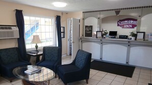 A Country Heart Inn reception area with a check-in counter, two armchairs, a glass table, and a window with curtains. - Country Hearth Inn & Suites Cartersville (Cartersville)