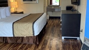 Quarto de hotel com uma cama, escrivaninha, televisão e banheiro visível através de uma porta aberta.