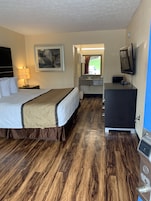 Habitación de hotel con cama, escritorio, televisión y baño visible a través de una puerta abierta.