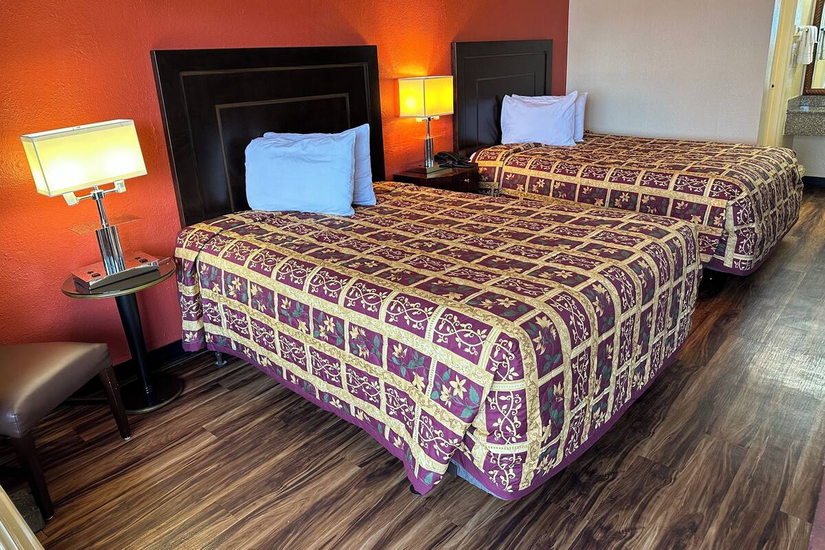 Ein Hotelzimmer mit zwei Betten, einem Nachttisch mit Lampe, einem Sessel und Holzboden.