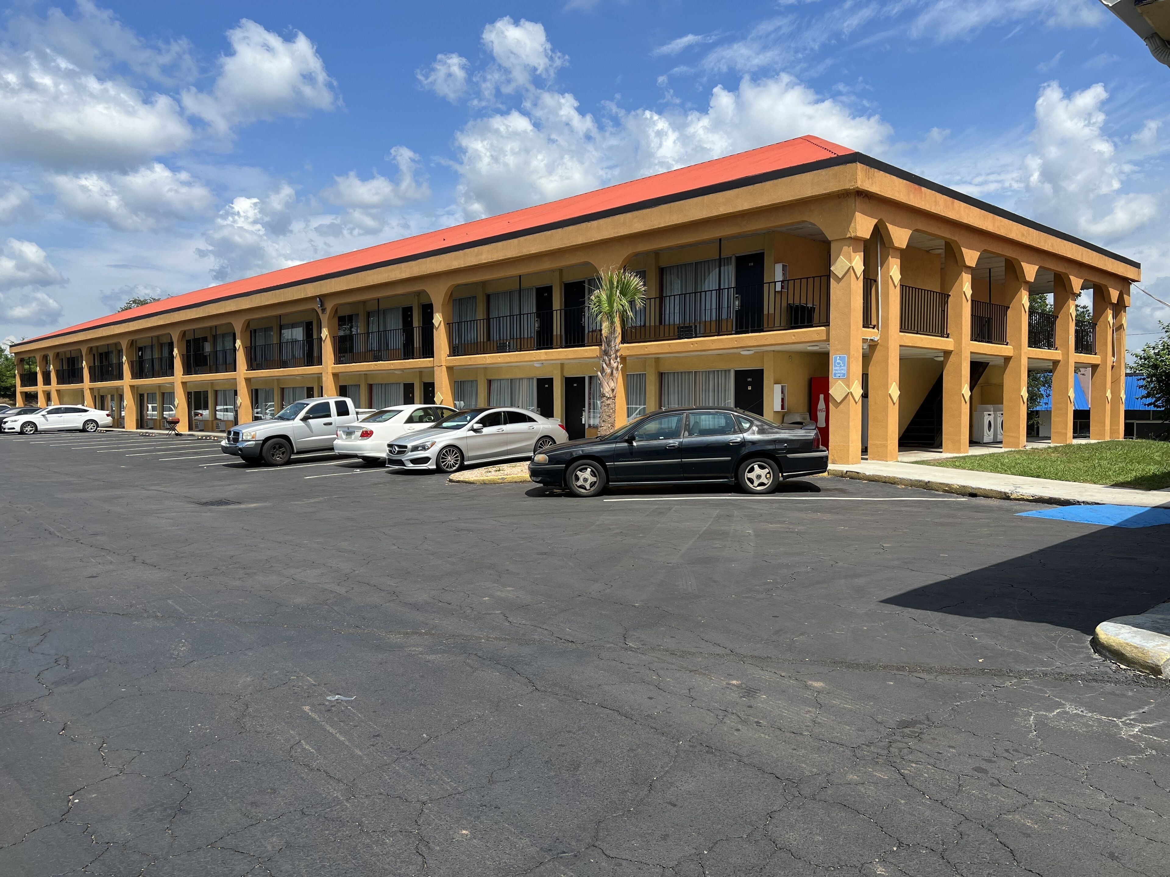 A multi-story hotel with a red roof and yellow facade, featuring a parking lot with several cars.