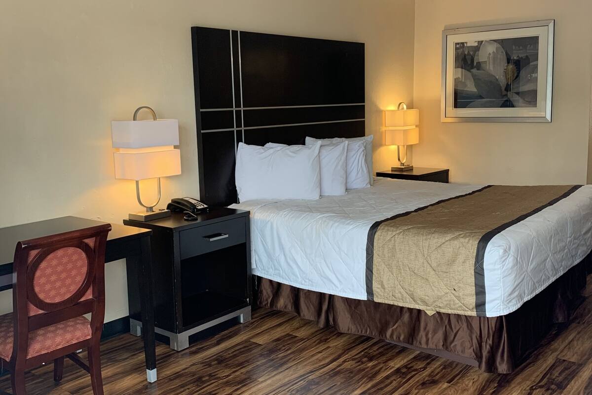Ein Hotelzimmer mit Bett, Nachttischen, Schreibtisch, Stuhl und einem gerahmten Bild an der Wand.