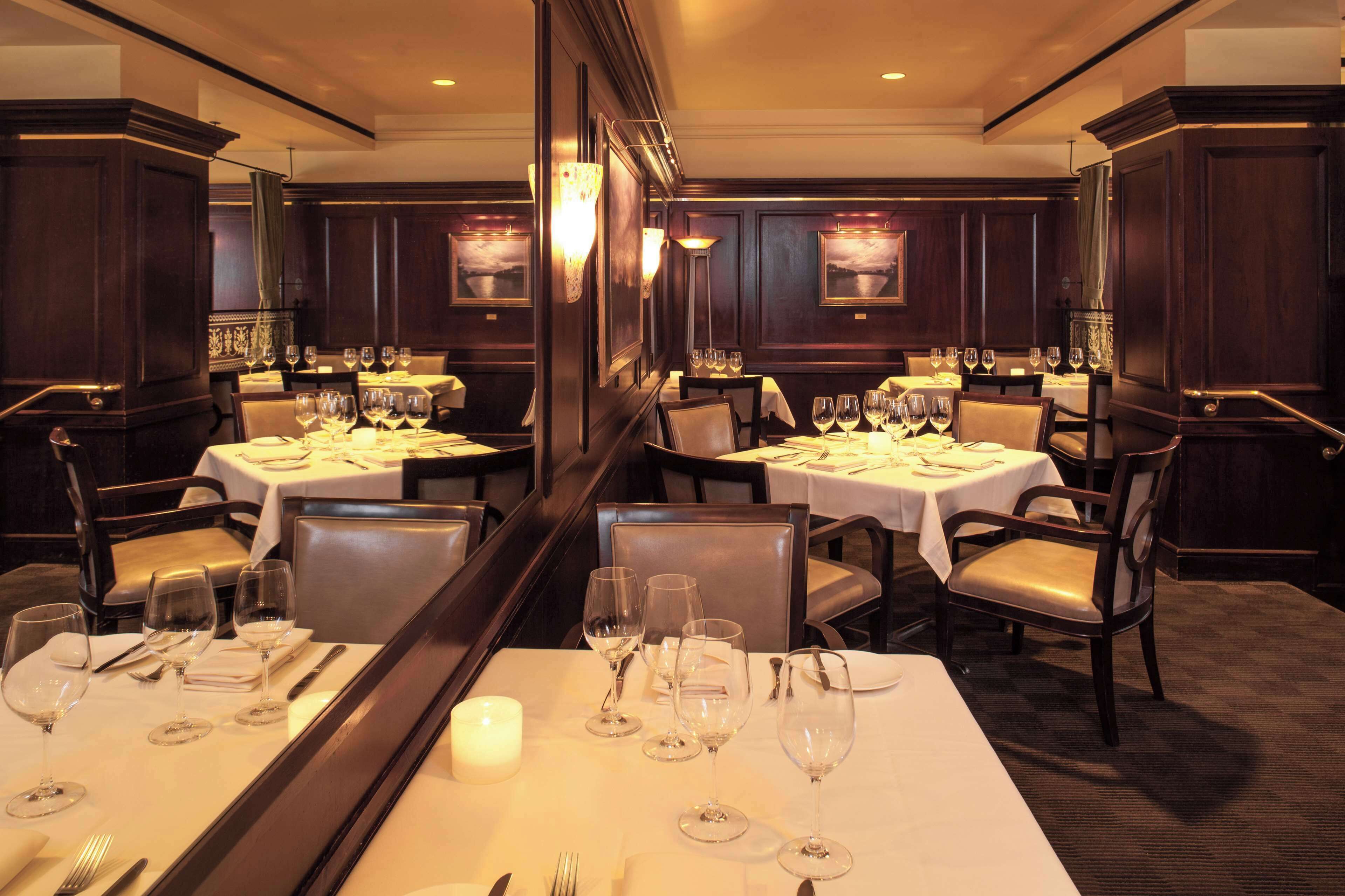 Een restaurant met meerdere gedekte tafels, elk voorzien van wijnglazen, bestek en kaarsen.
