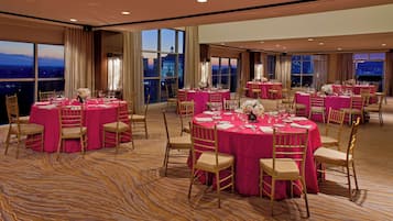 A large banquet hall with round tables covered in pink tablecloths, gold chairs, and floral centerpieces.