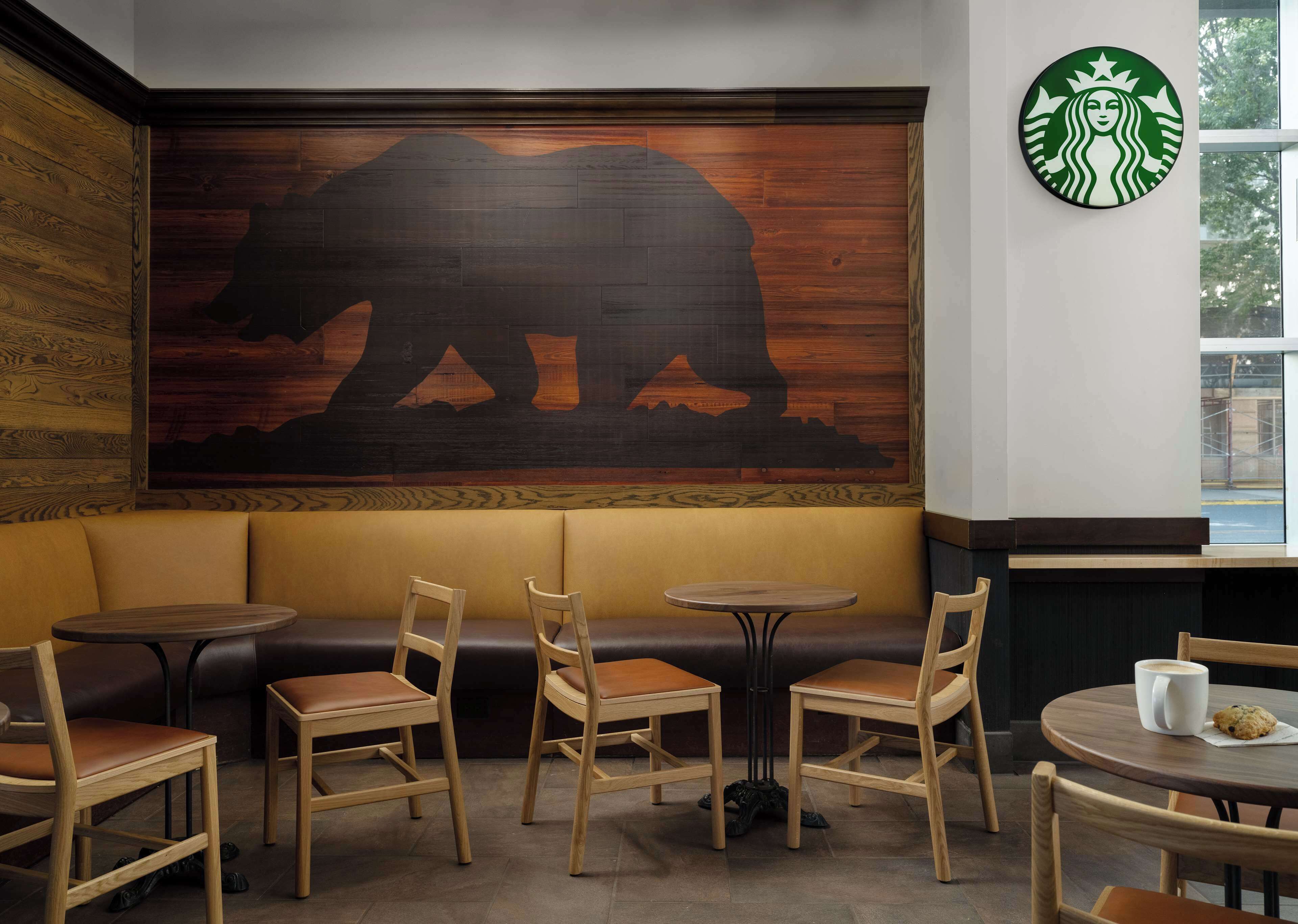 Ein gemütlicher Sitzbereich mit Holzbänken und -tischen, einem großen Bären-Wandgemälde und dem Starbucks Logo.