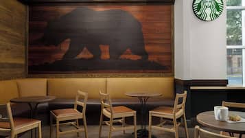 Un rincón acogedor con bancos y mesas de madera, un gran mural de un oso en la pared, y el logotipo de Starbucks.