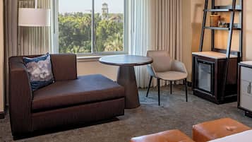 Habitación de hotel con sofá, sillón, mesa redonda y minibar.