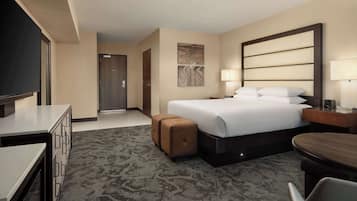 A hotel room with a bed, a desk, a TV, a lamp, and a door.