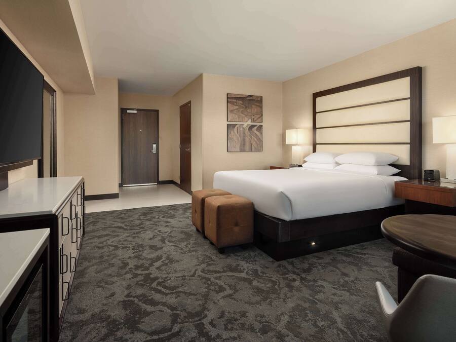 A hotel room with a bed, a desk, a TV, a lamp, and a door.
