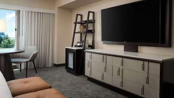 Une chambre d’hôtel dotée d’un grand téléviseur à écran plat fixé au mur, d’un petit bureau avec une chaise, d’un canapé et d’un mini-bar.