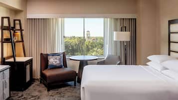 A hotel room with a bed, a chair, a small table, a desk, and a lamp.