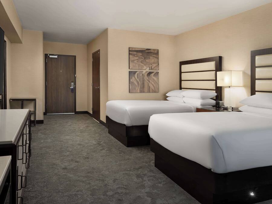 A hotel room with two beds, a desk, a chair, a door, and a wall-mounted artwork.