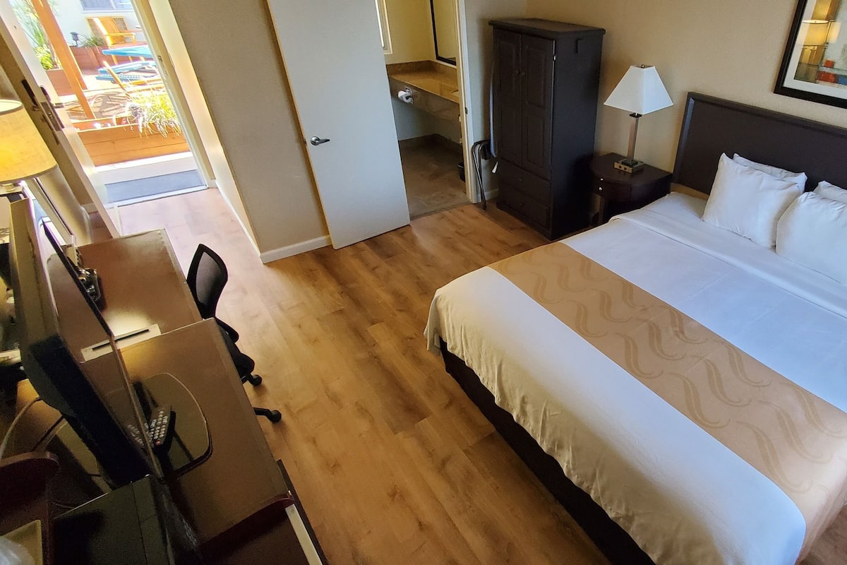 Une chambre d’hôtel avec un grand lit, un bureau avec un ordinateur, une armoire, une table de chevet avec une lampe et une fenêtre donnant sur l’extérieur.