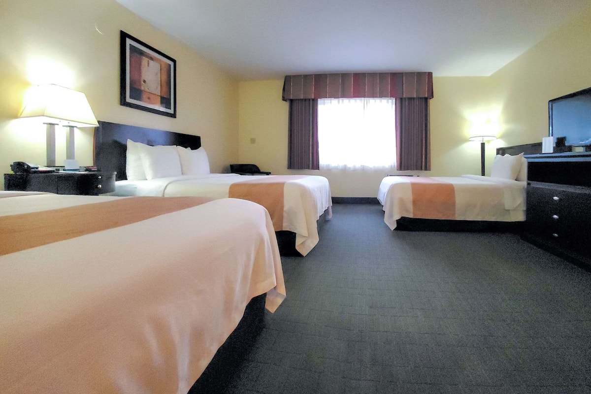 Une chambre d’hôtel avec deux lits, un bureau, une chaise, une lampe et un téléviseur.