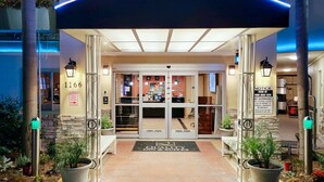 L’entrée d’un hôtel, avec une porte en verre, une enseigne indiquant le numéro « 1166 », et un panneau d’information concernant le stationnement.