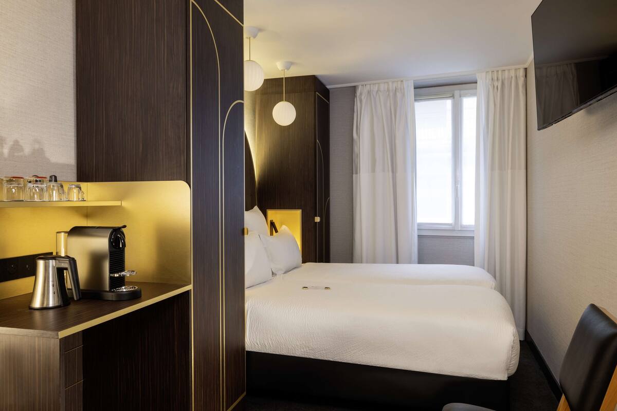 Una habitación de hotel con cama, escritorio con cafetera y televisión montada en la pared.