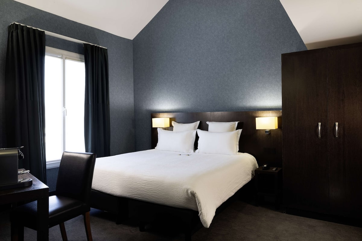 Habitación de hotel con una cama grande, dos lámparas de noche, un escritorio con una computadora portátil, una silla y un armario.
