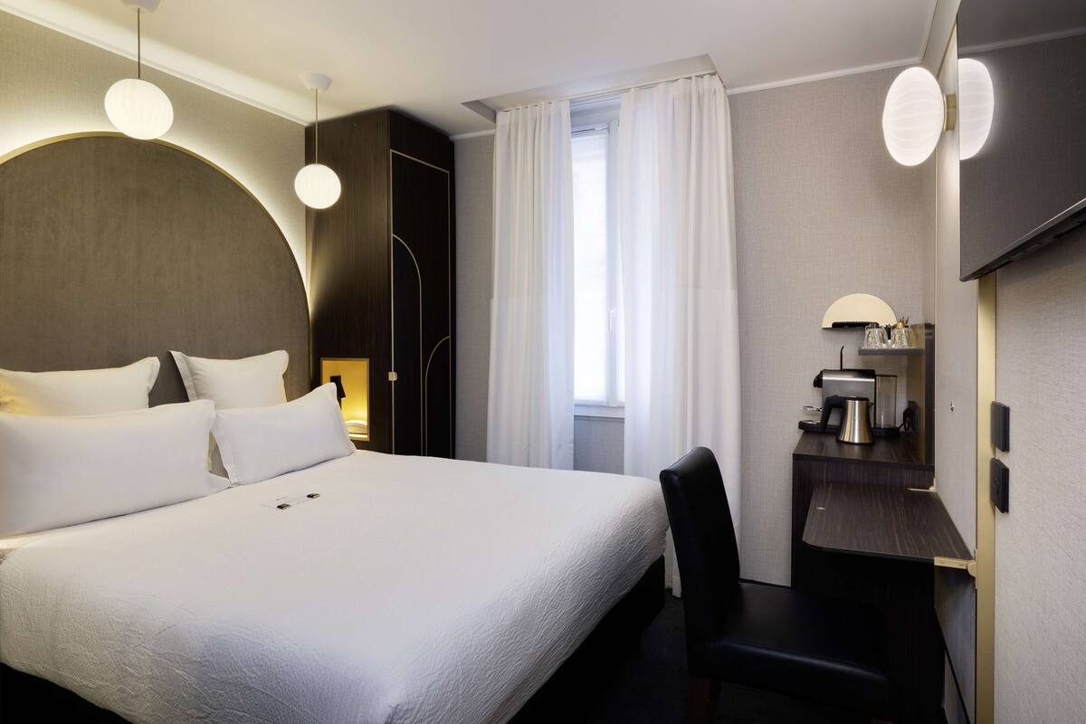 Una habitación de hotel con una cama grande, un escritorio con cafetera y una silla.