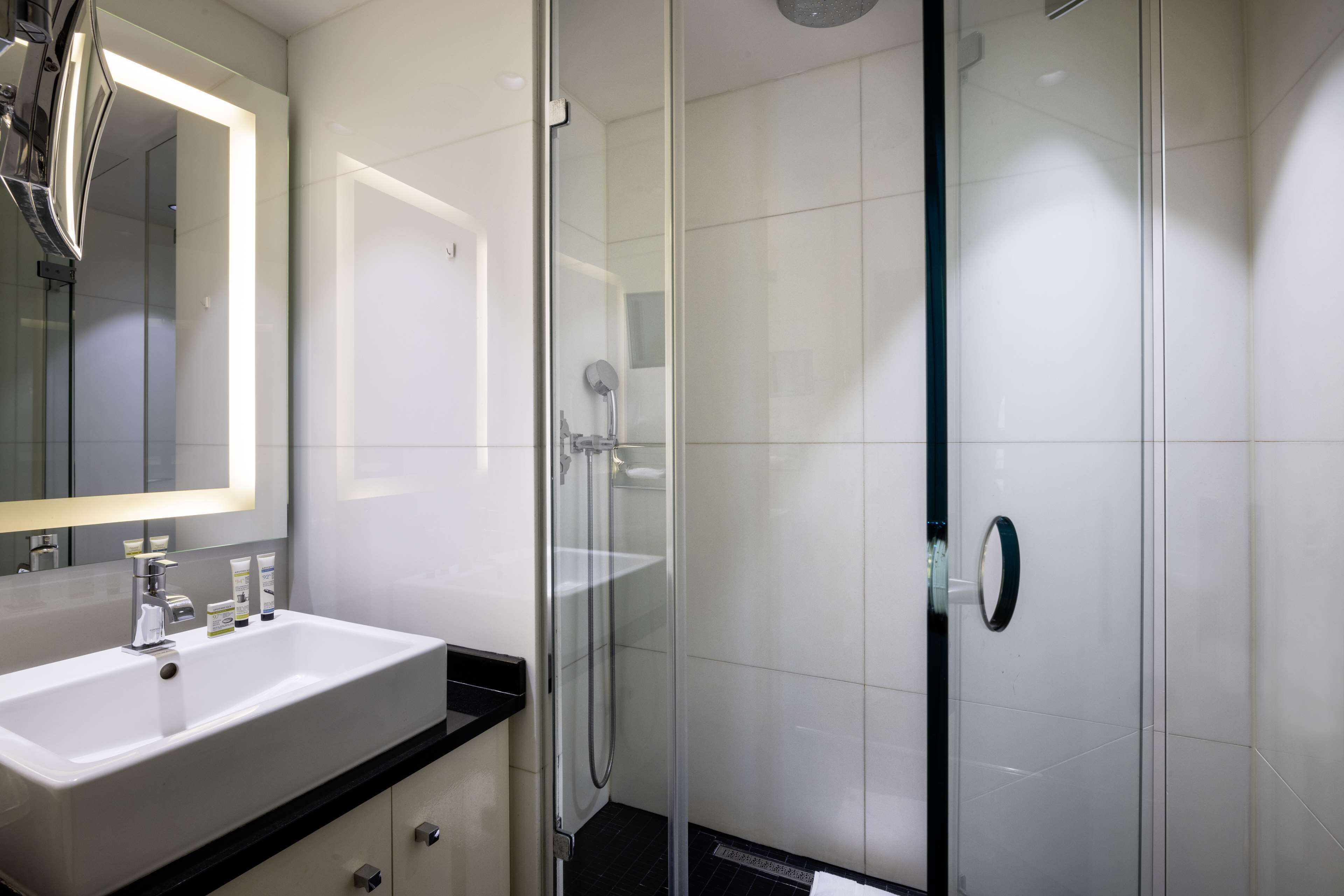 Un baño moderno con un lavamanos blanco, cabina de ducha con mampara de vidrio y un espejo grande.