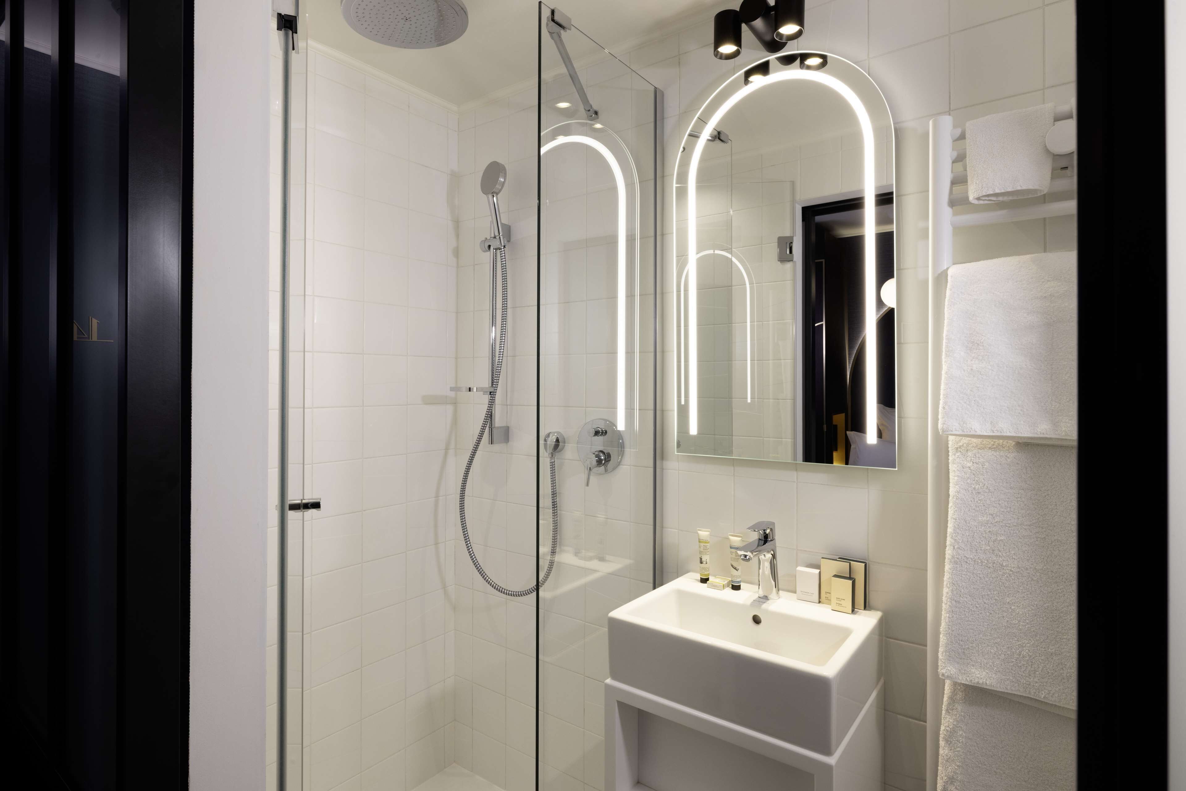 Une salle de bain moderne dotée d’une douche à parois de verre, d’un lavabo blanc et d’un miroir avec éclairage intégré.