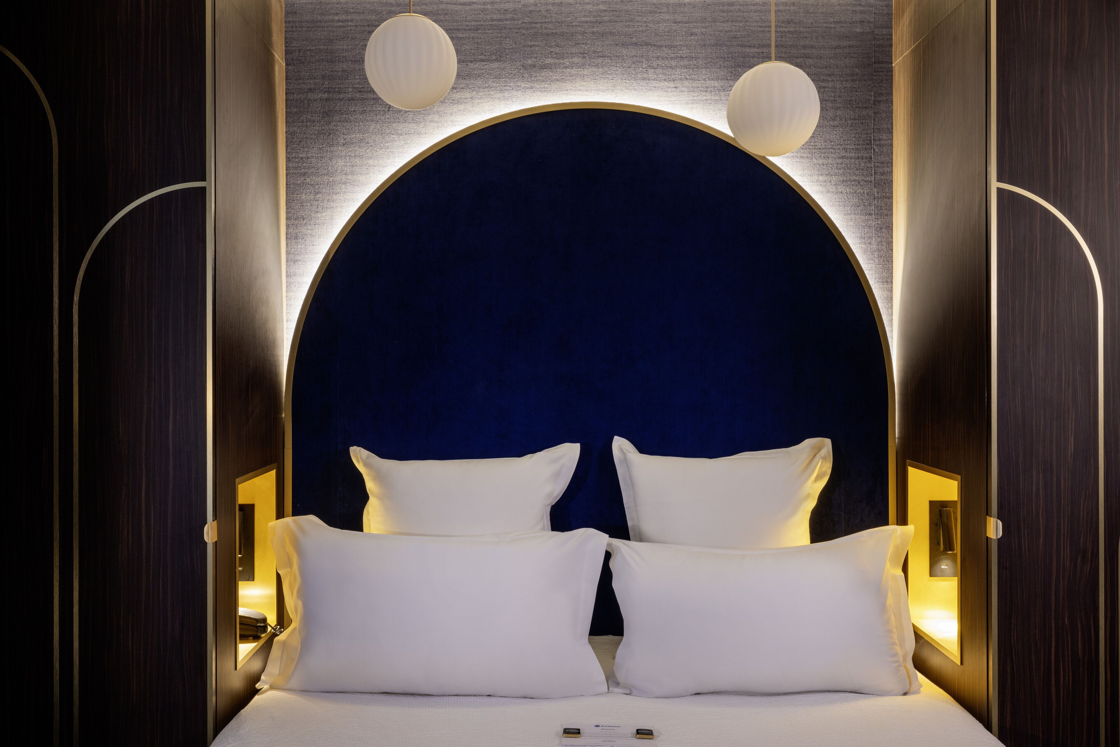 A modern hotel room with a large bed, two bedside tables, and a circular headboard.