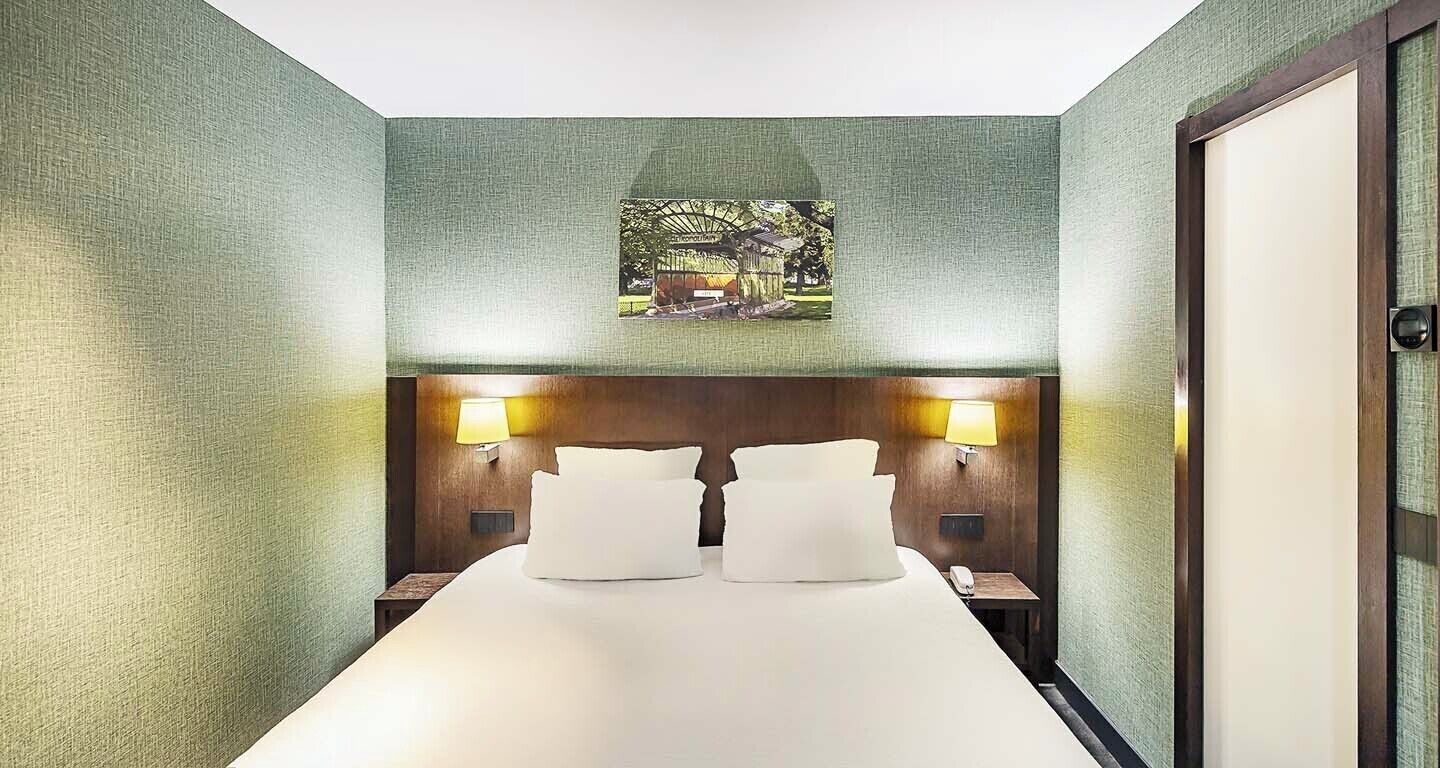 A hotel room with a large bed, two bedside lamps, a nightstand, and a framed picture on the wall.