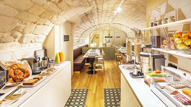 A cozy café with stone walls, a central seating area, and various food and drink stations.