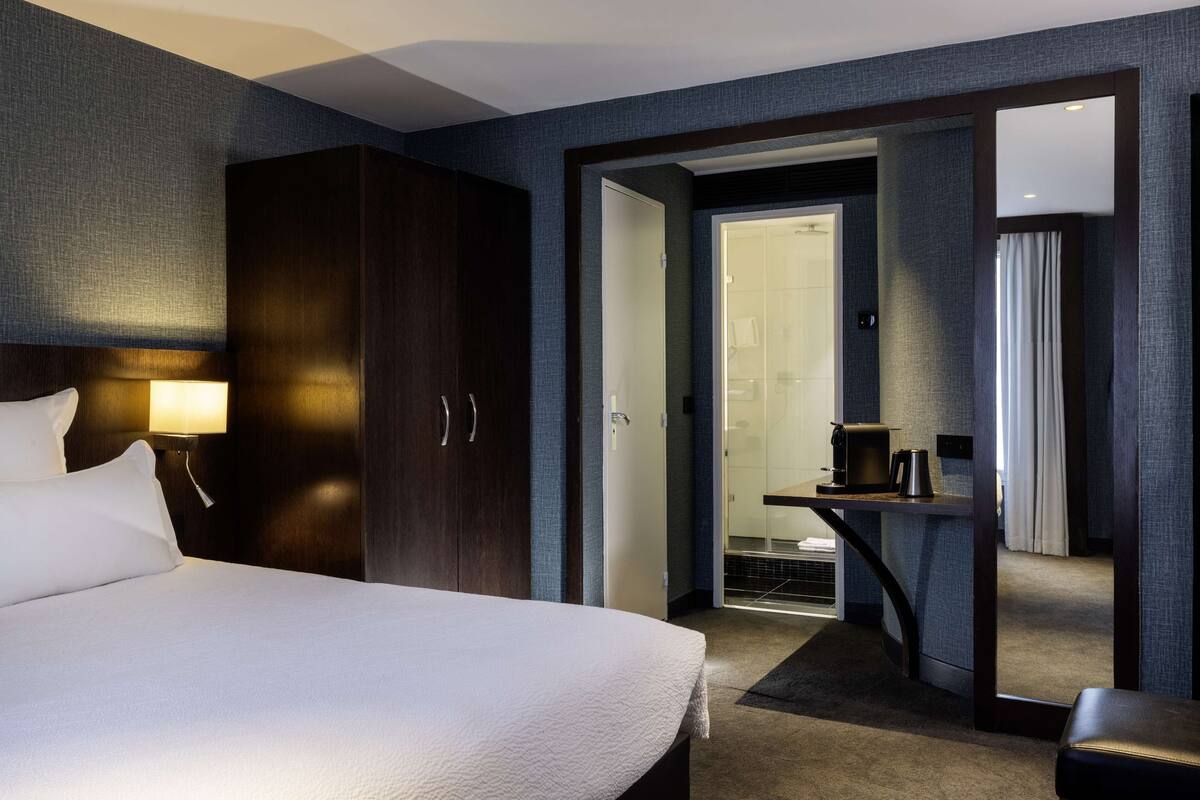 Una habitación de hotel con una cama grande, un escritorio con cafetera y un armario.