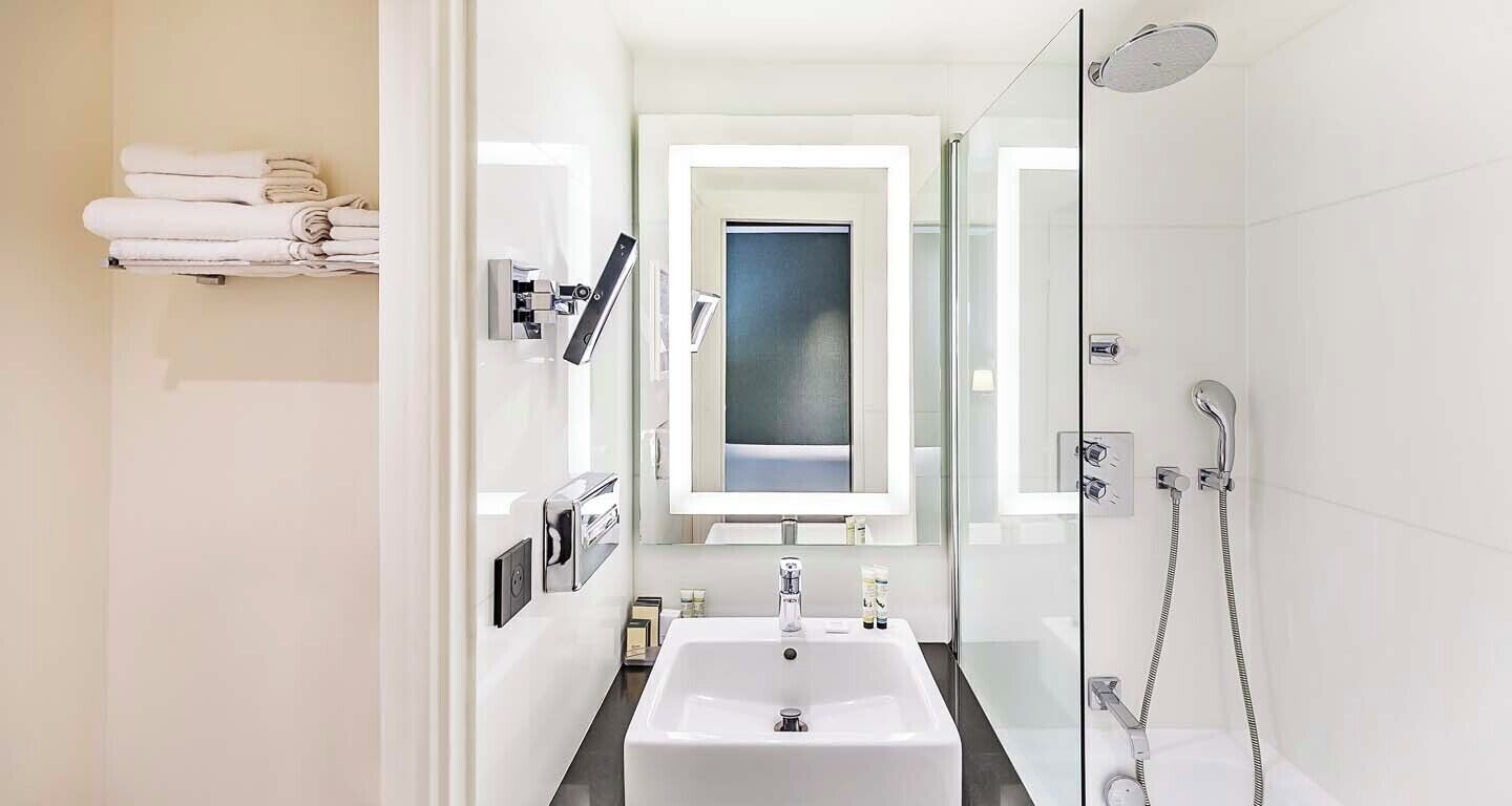 A modern bathroom with a white sink, a glass shower enclosure, and a towel rack with folded towels.