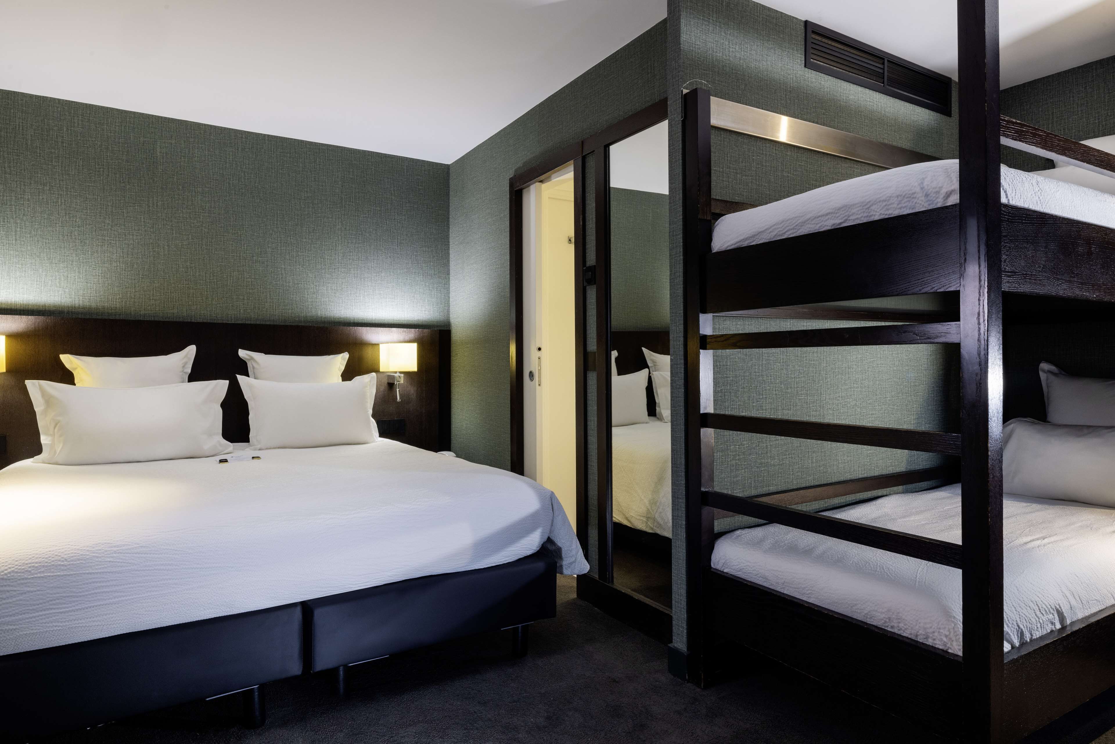 Habitació d'hotel amb un llit gran, un llit superposat i una porta corredissa.