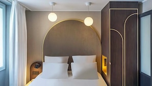 A modern hotel room with a large bed, two bedside lamps, and a large window with curtains.